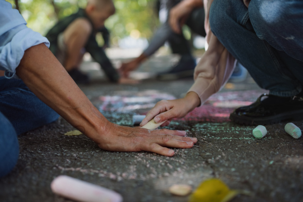 A close-up of senior couple with grandchildren drawing with chalks on pavement outdoors in park.