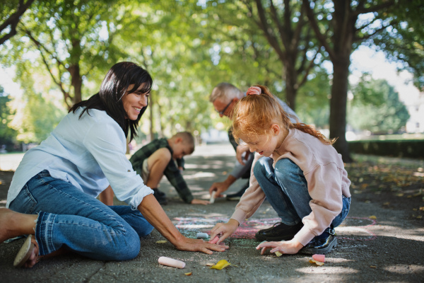 A senior couple with grandchildren drawing with chalks on pavement outdoors in park.