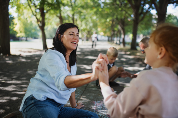 A senior couple with granddaughter drawing with chalks on pavement outdoors in park.