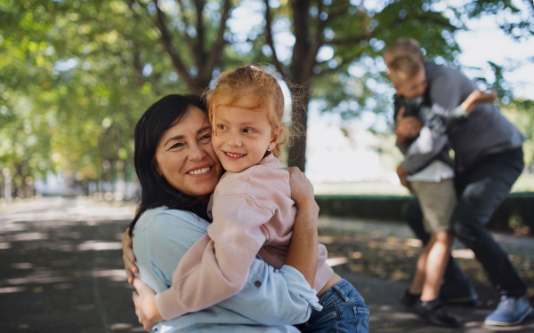 A happy little girl hugging her grandmother outdoors in park.