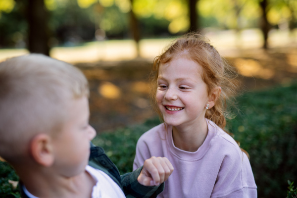 A happy little girl with freckles and red hair having fun with her brother and smiling outdoors in park.