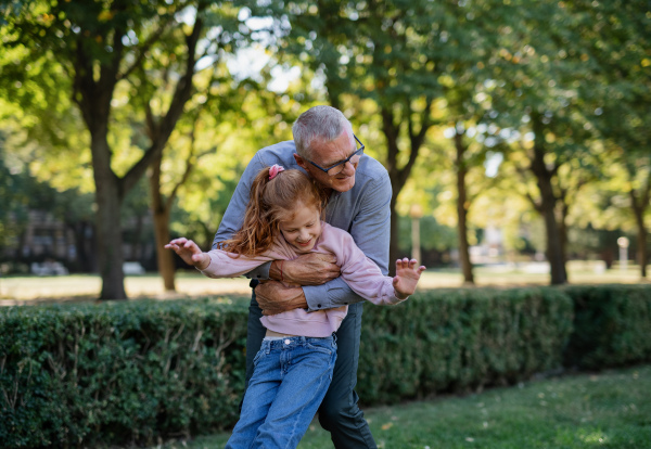 A happy grandfather hugging his little granddaughter outdoors in park.