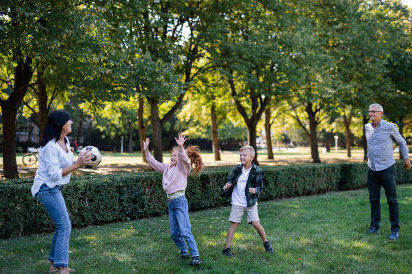 Happy little children with grandparents playing with ball outdoors in a park