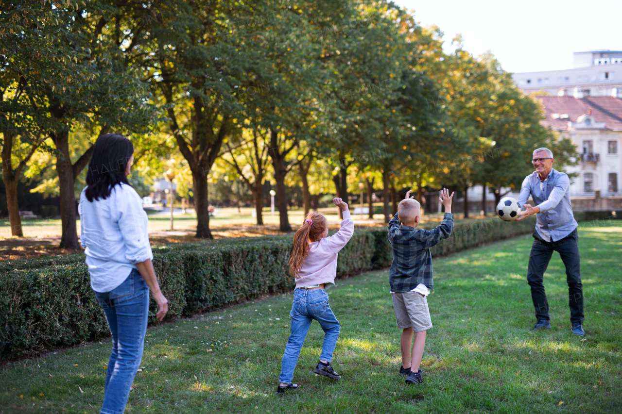 Happy little children with grandparents playing with ball outdoors in a park