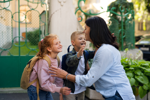 Happy schoolchildren hugging their grandmother waiting for her after school outdoors in a street.