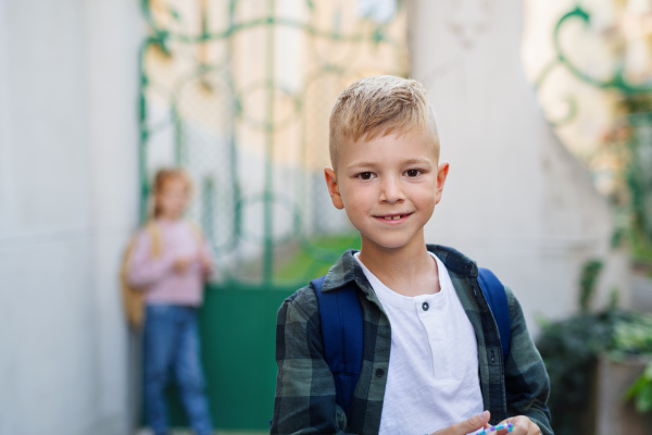 A happy little schoolboy looking at camera in front of school.