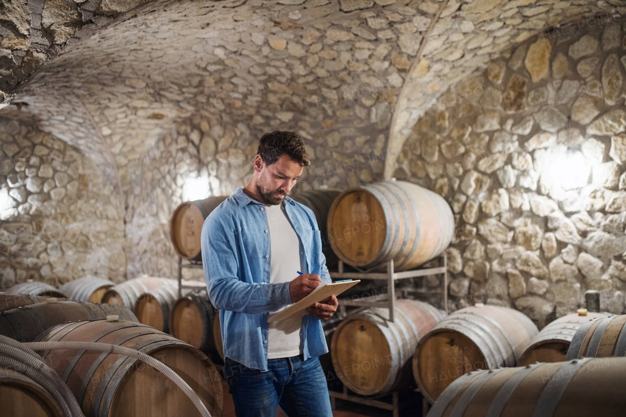 Man worker with clipboard indoors, wine making concept. Copy space.