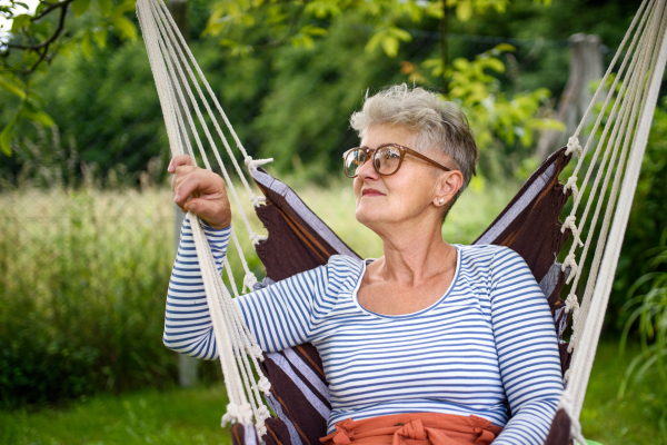 Front view portrait of happy senior woman sitting outdoors on hanging swing chair in garden, relaxing.