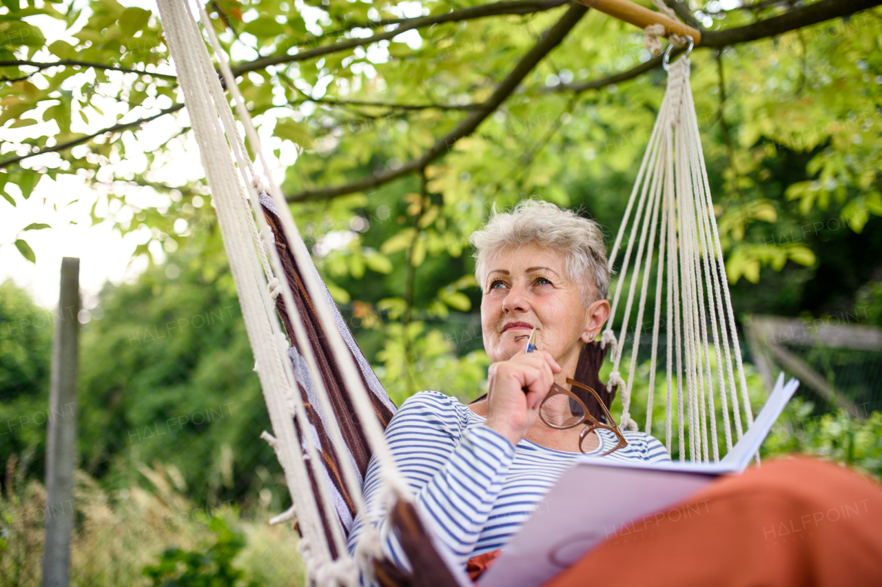 Front view portrait of happy senior woman sitting outdoors on hanging swing chair in garden, relaxing.