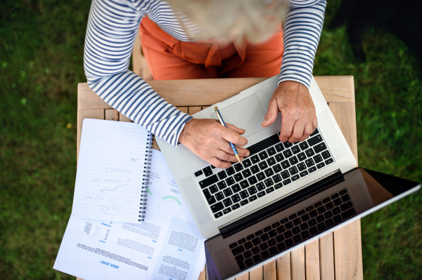 Top view of unrecognizable senior woman with laptop working outdoors in garden, home office concept.