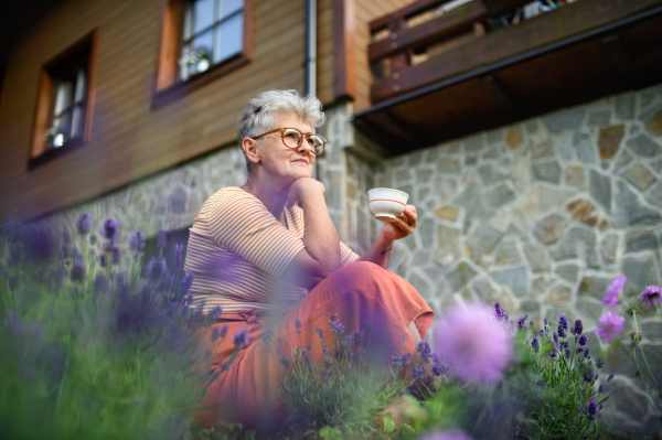 Portrait of senior woman sitting and resting outdoors in garden, holding cup of coffee.