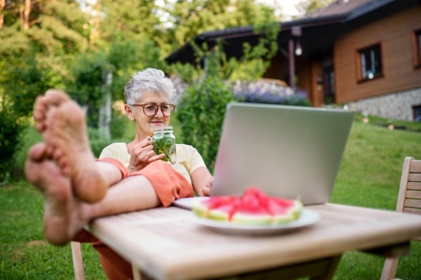 Happy senior woman with laptop and feet on desk working outdoors in garden, home office concept.