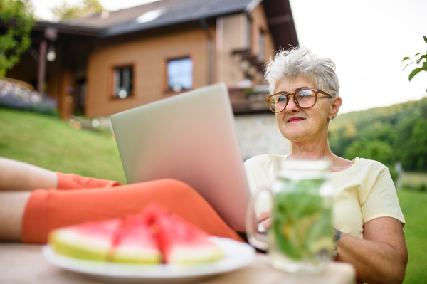 Happy senior woman with laptop and feet on desk working outdoors in garden, home office concept.