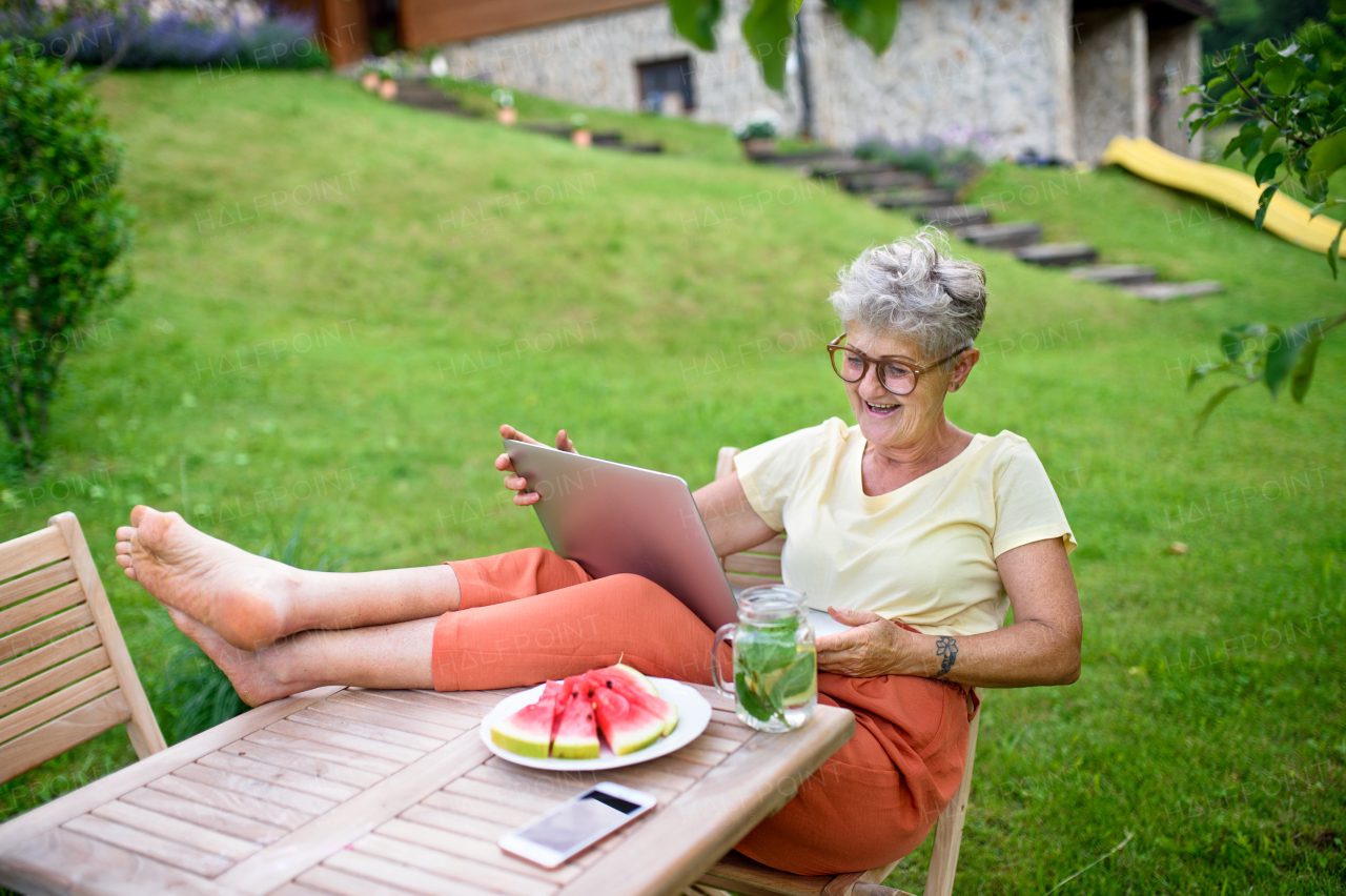 Happy senior woman with laptop and feet on desk working outdoors in garden, home office concept.