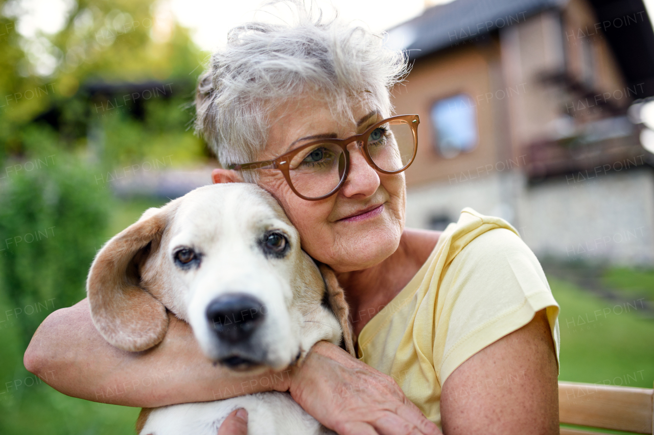 Portrait of senior woman sitting and resting outdoors in garden, holding pet dog.