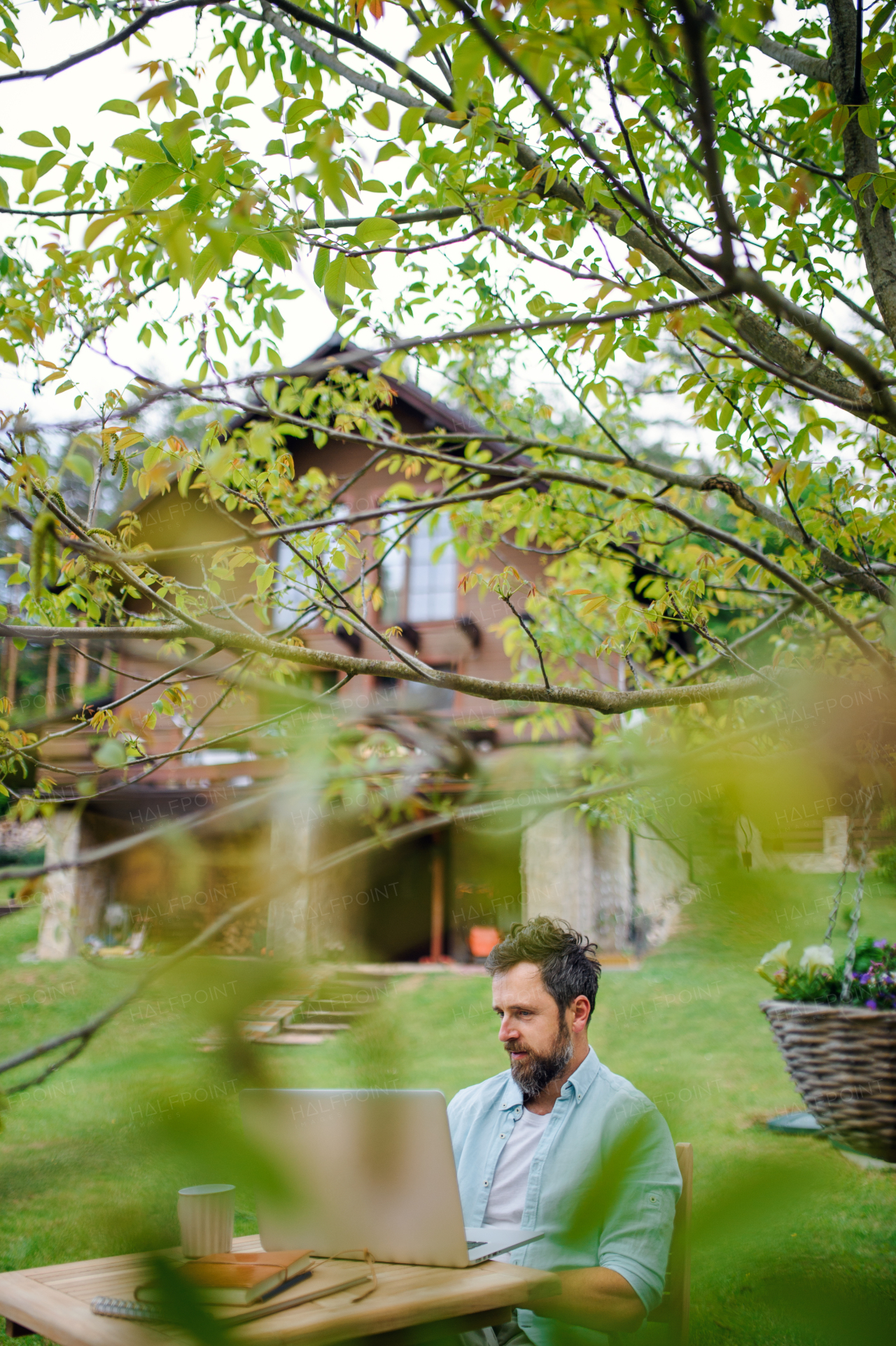 Side view of mature man with laptop working outdoors in garden, home office concept.