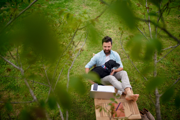 Top view of business man with dog and laptop working outdoors in garden, home office concept.