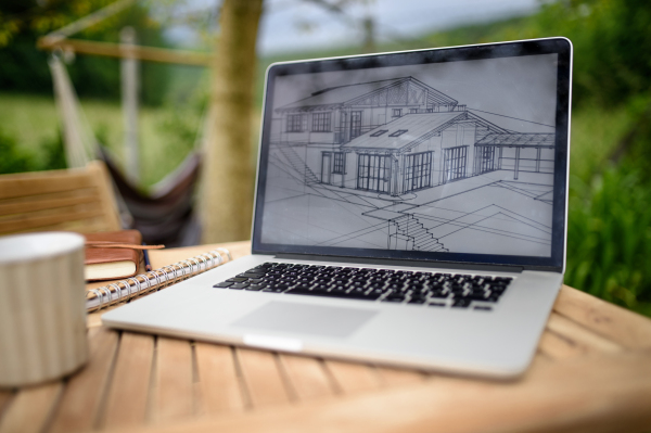 Laptop with blueprints and coffee on desk outdoors in garden, home office concept.