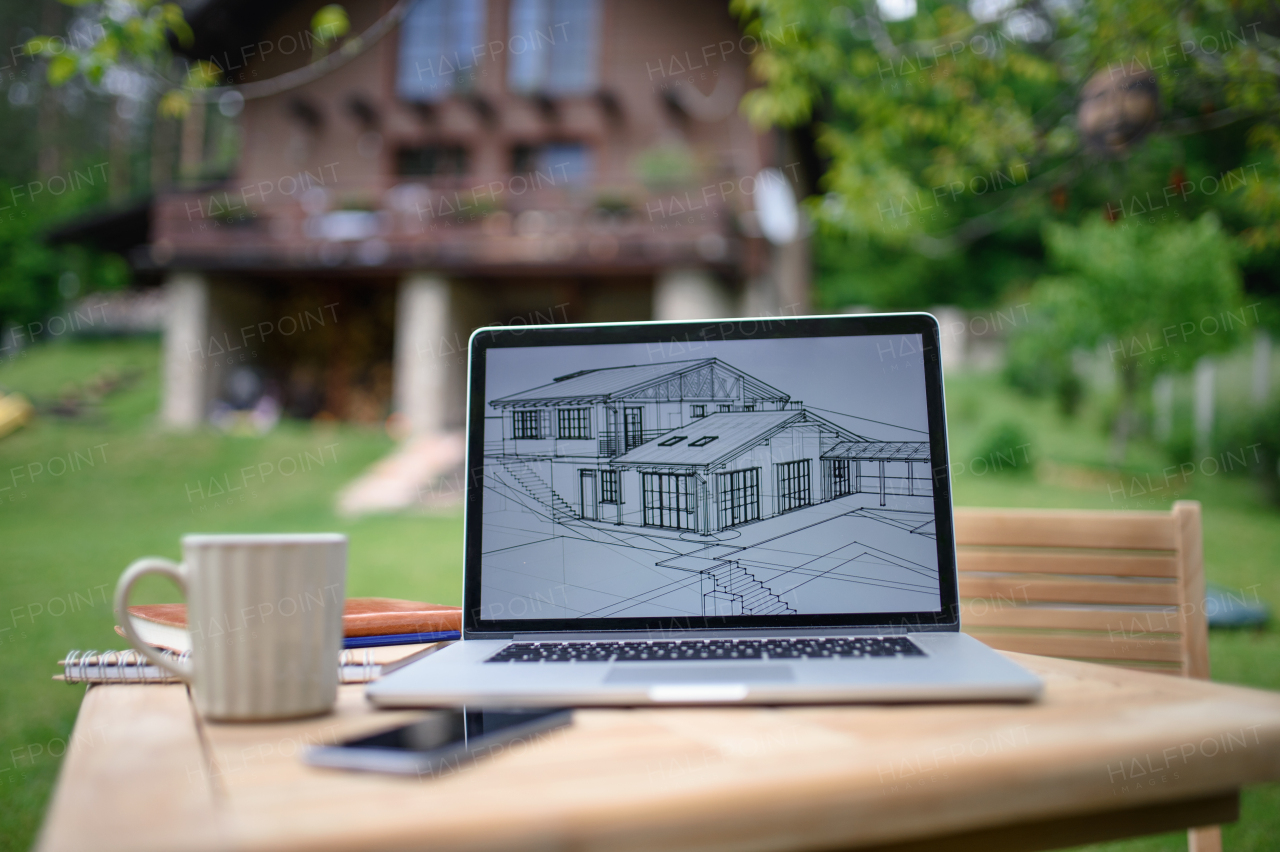 Laptop with blueprints and coffee on desk outdoors in garden, home office concept.