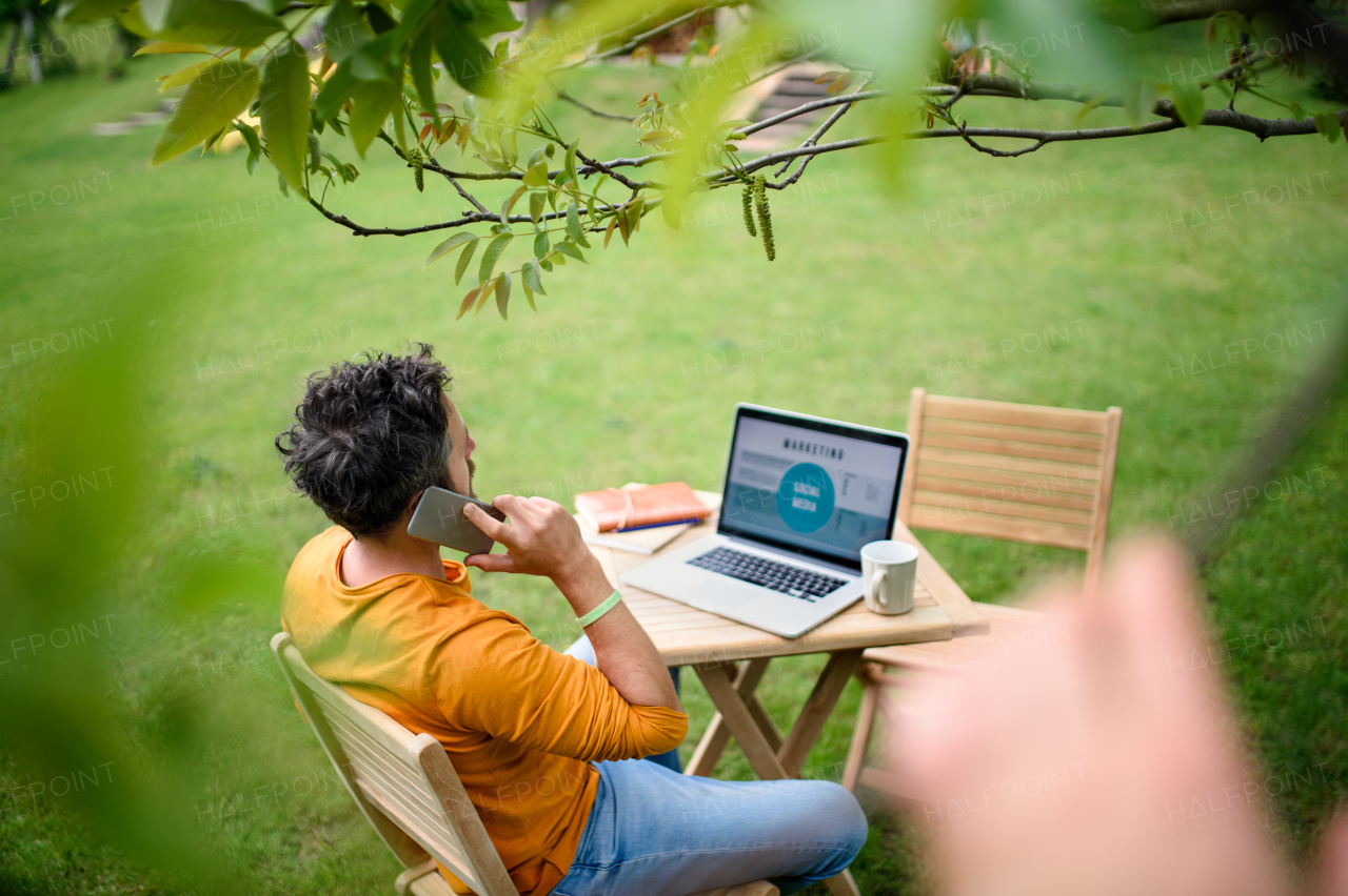 High-angle view of mature man with laptop and smartphone working outdoors in garden, home office concept.