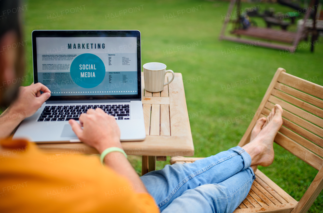 Top view of unrecognizable man with laptop working outdoors in garden, home office concept.