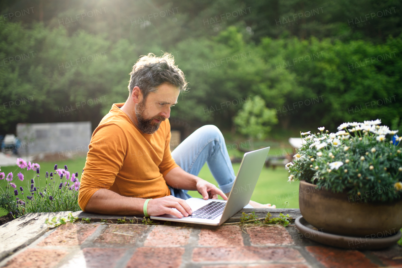 Happy mature man with laptop working outdoors in garden, home office concept.