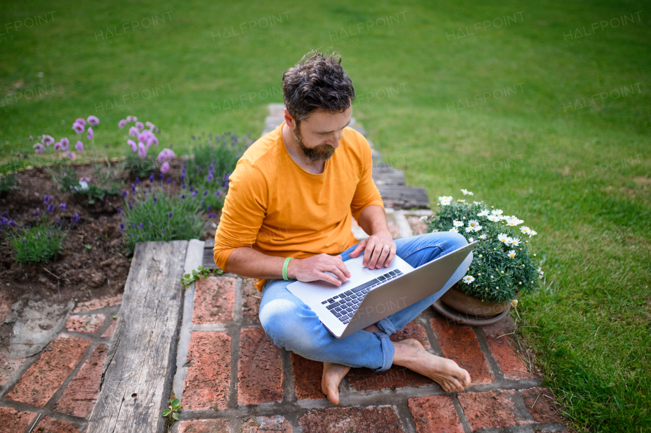 Top view of mature man with laptop working outdoors in garden, home office concept.