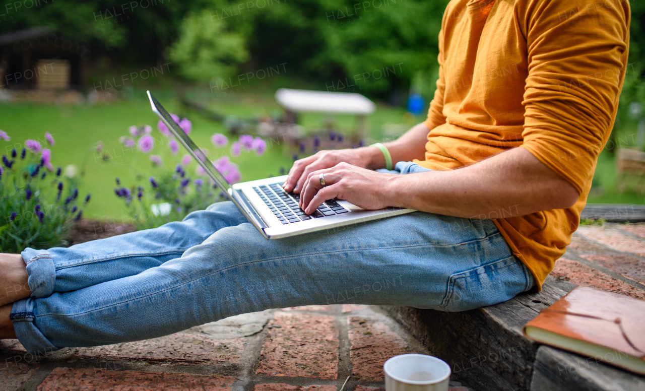 Midsection of unrecognizable man with laptop working outdoors in garden, home office concept.