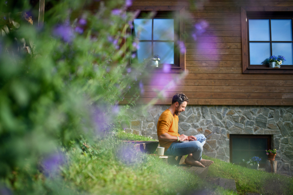 Portrait of mature man with laptop working outdoors in garden, home office concept.