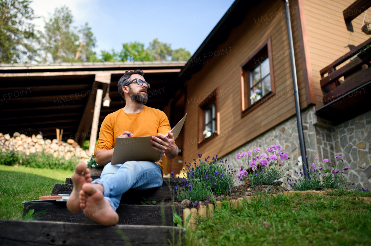 Portrait of mature man working outdoors in garden, home office concept.