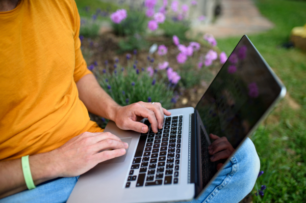 Midsection of unrecognizable man with laptop working outdoors in garden, home office concept.