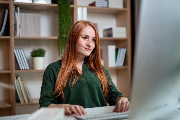 A young businesswoman sitting at the desk indoors in office, using computer.