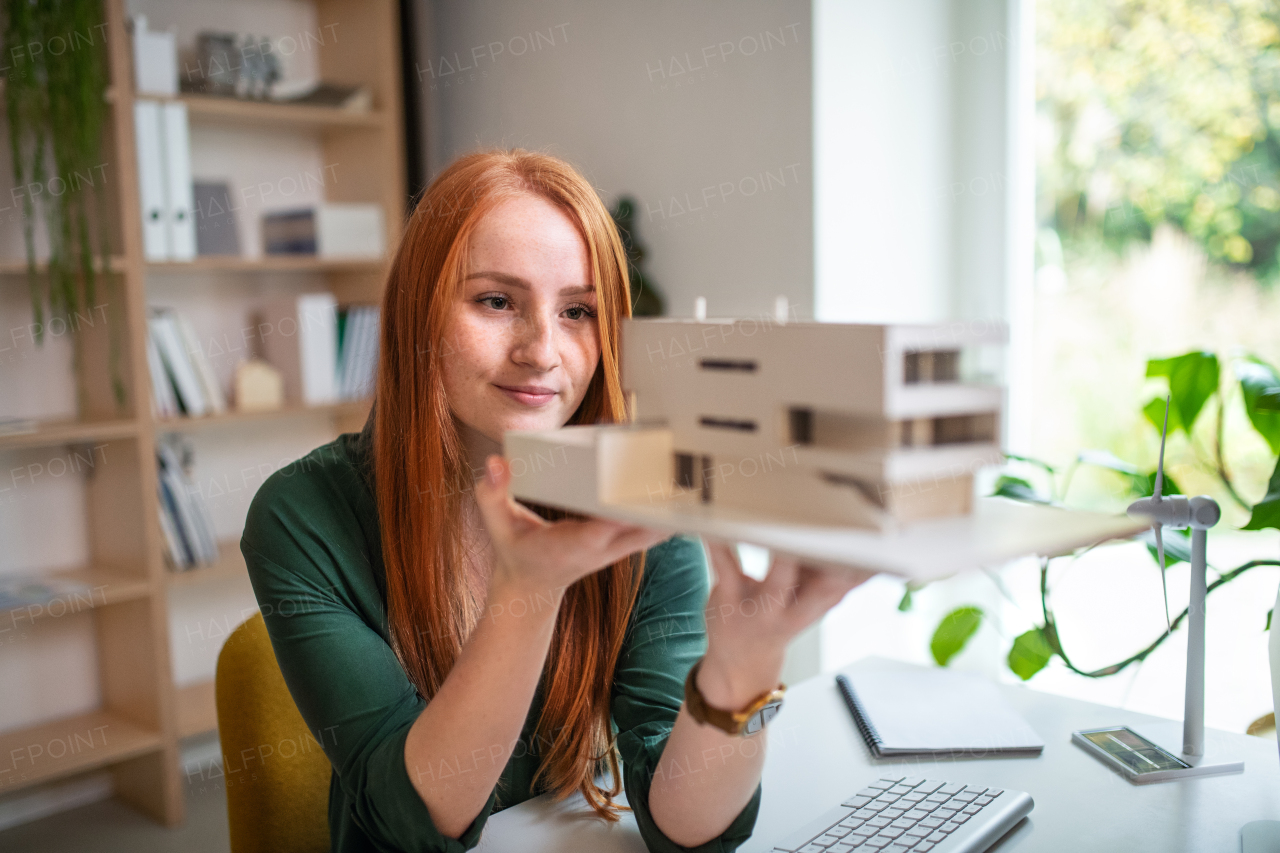 Architect with model of a house sitting at the desk indoors in office, working.