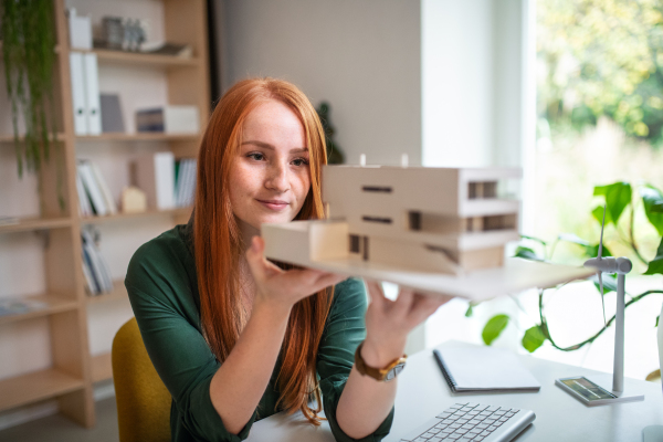 Architect with model of a house sitting at the desk indoors in office, working.