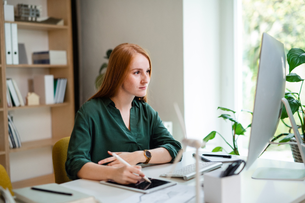 A young businesswoman sitting at the desk indoors in office, using computer.