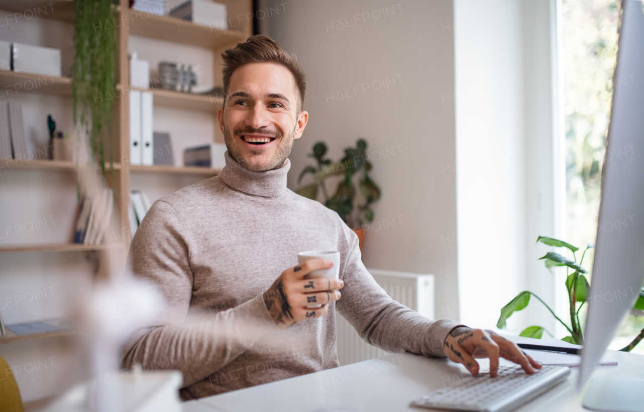 A young businessman sitting at the desk indoors in office, using computer.