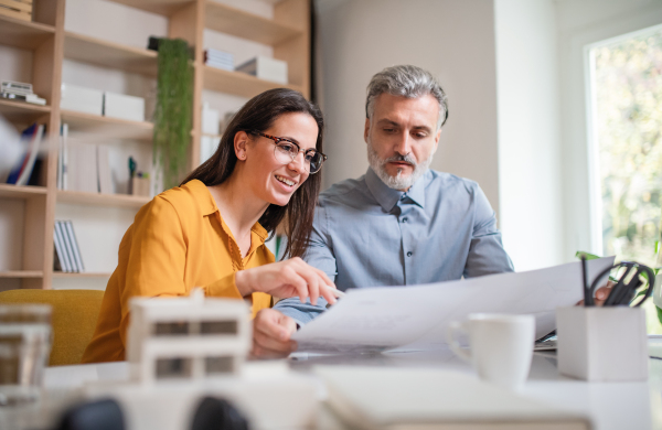 Mature architects with model of house sitting at the desk indoors in office, working.