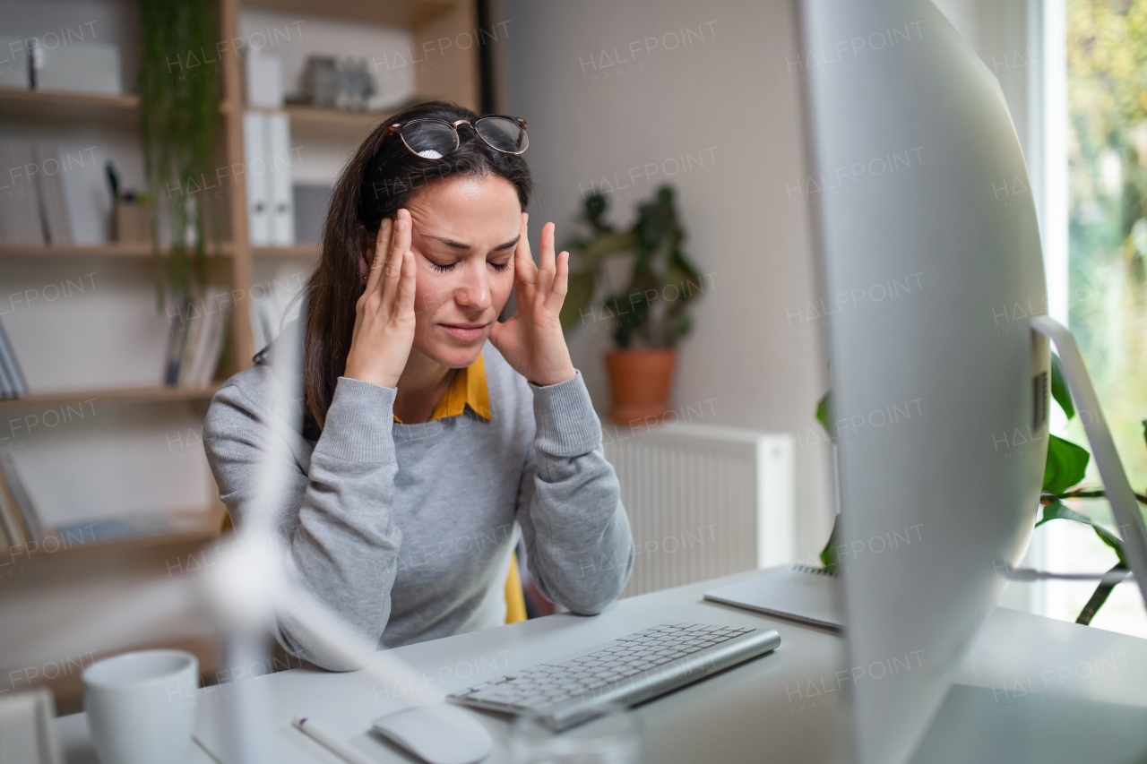 Tired businesswoman with headache at the desk indoors in office, feeling pain.