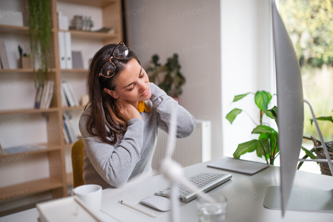 A businesswoman at the desk indoors in office, feeling pain in neck.