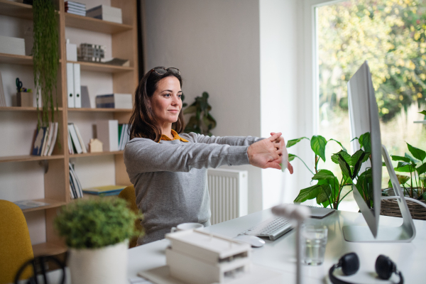 An attractive businesswoman sitting indoors in office, stretching.