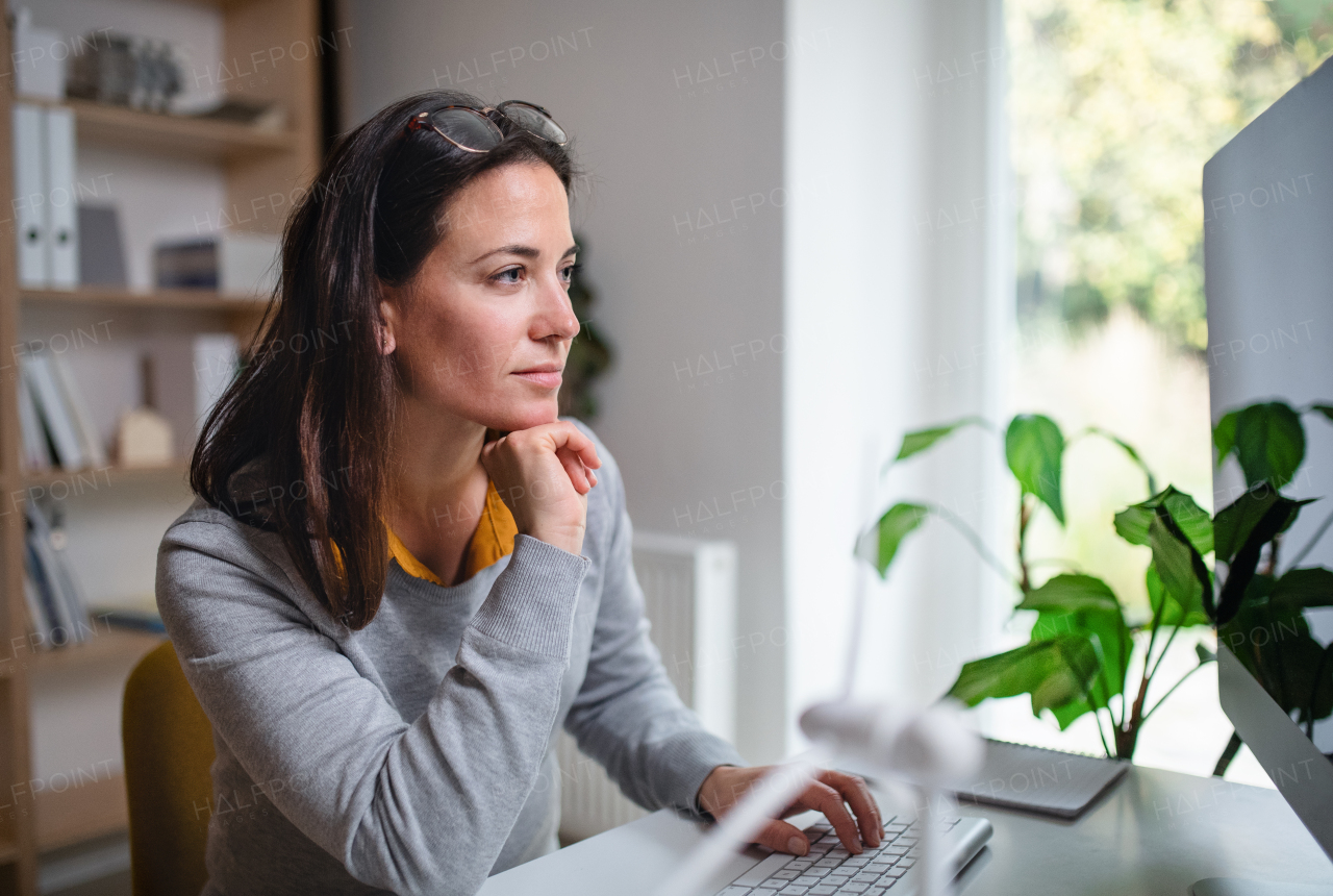 A businesswoman sitting at the desk indoors in office, using computer.