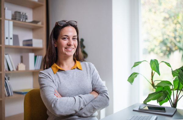 Attractive businesswoman sitting indoors in office, looking at camera. Copy space.