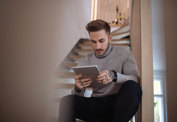 Young man sitting on stairs indoors in office, using tablet. Copy space.