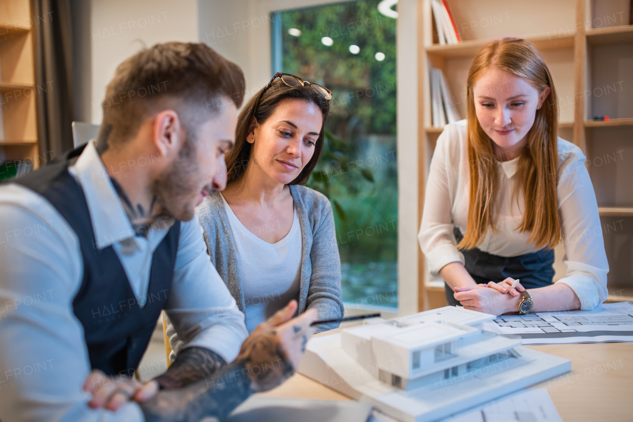 Group of architects with model of house sitting at the desk indoors in office, working.