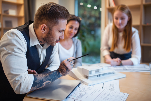 Group of architects with model of house sitting at the desk indoors in office, working.