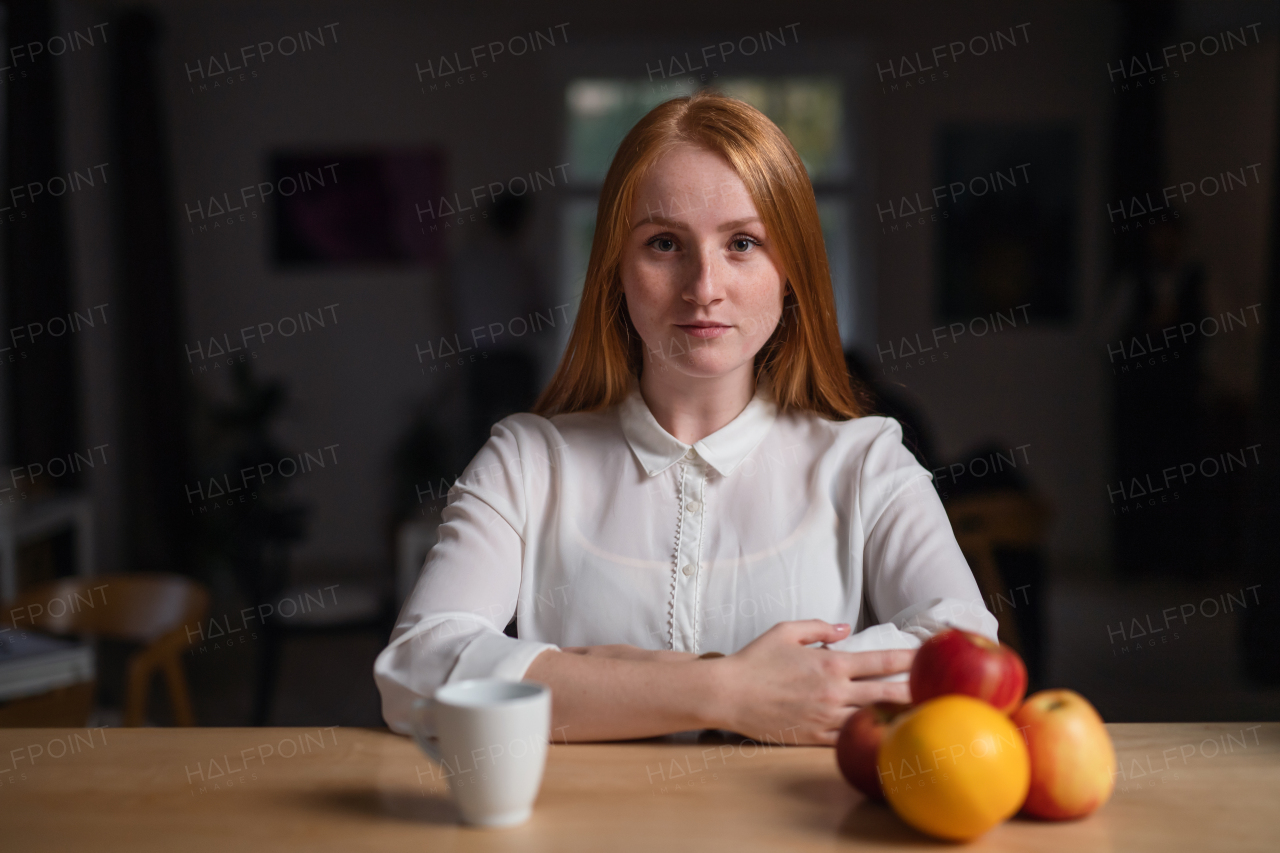 A young businesswoman sitting at the desk indoors in office, looking at camera.