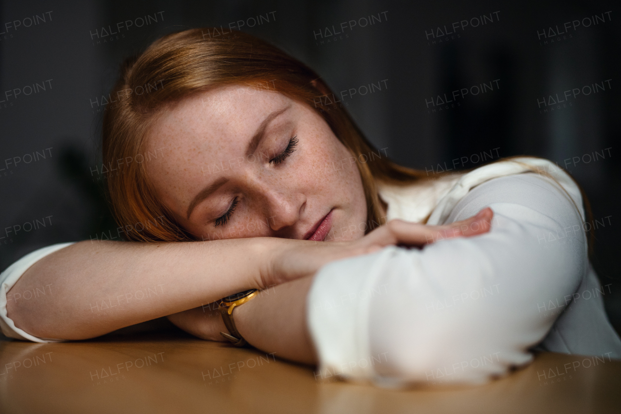 A tired young businesswoman sitting at the desk indoors in office, sleeping.