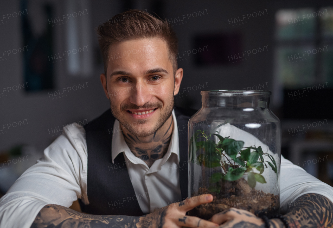 A businessman with plant terrarium sitting at the desk indoors in green office.