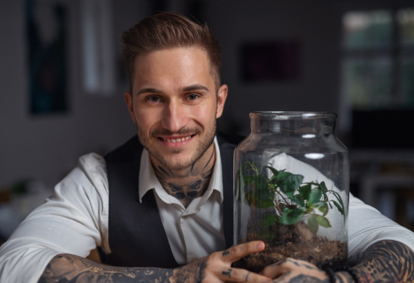 A businessman with plant terrarium sitting at the desk indoors in green office.