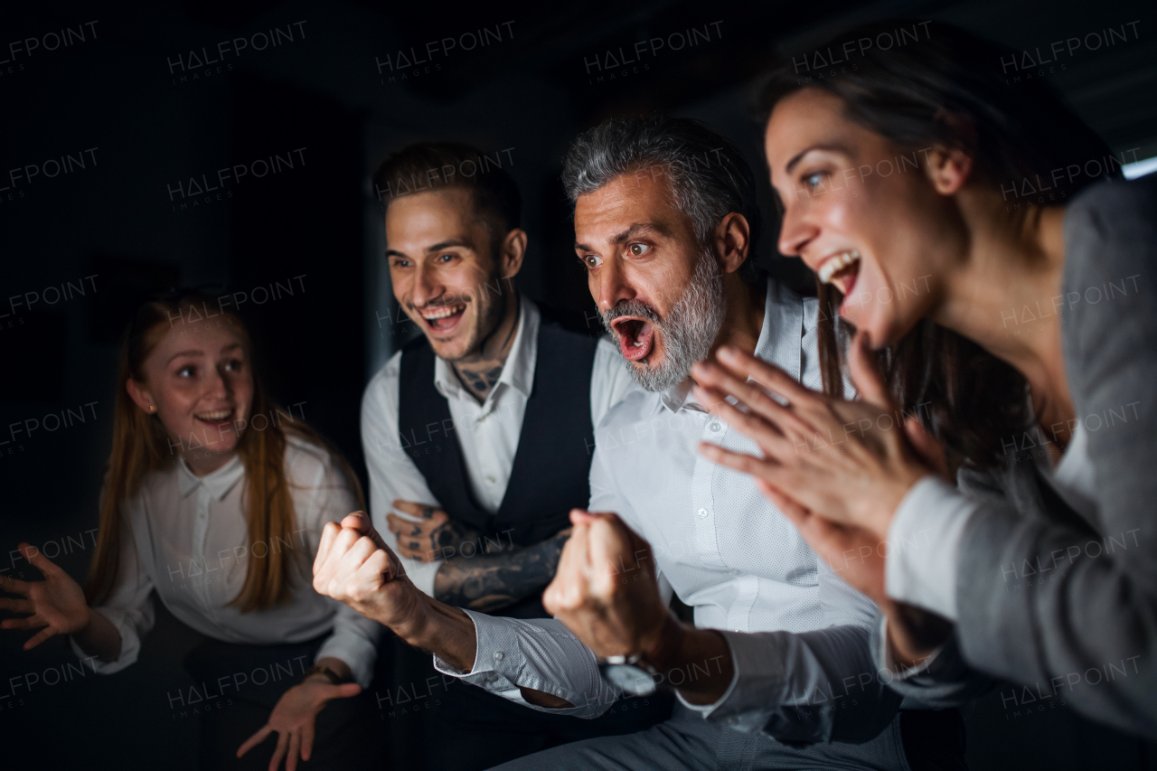 Group of cheerful businesspeople expressing excitement indoors in office, working late.